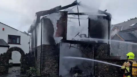 Mid and West Wales Fire and Rescue Service Firefighter spraying a hose jet at the garage in Swansea