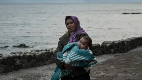 AFP A migrant woman carries a toddler on Lesbos