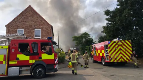 Shaun Whitmore/BBC Firefighters tackling the flames at the site in Weeting