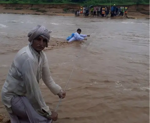 AFP This photo taken on July 25, 2017 shows Indian men trying to cross flood waters in Deesa municipality, which has been hit by severe flooding along the Banas River in northern Gujarat state in western India