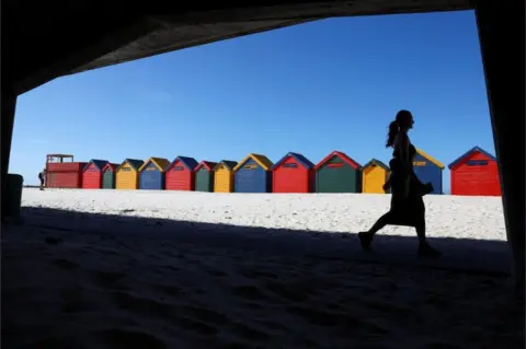 ESA ALEXANDER/REUTERS A woman walks past colourful beach huts.