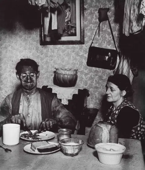 Bill Brandt A photograph of a miner eating a meal at a dinner table as a woman looks on