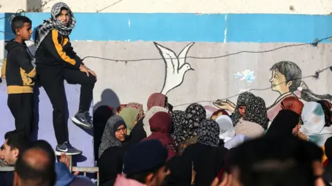 NurPhoto Palestinians queue for food aid at a UN distribution centre in Deir al-Balah, in central Gaza (10 December 2023)