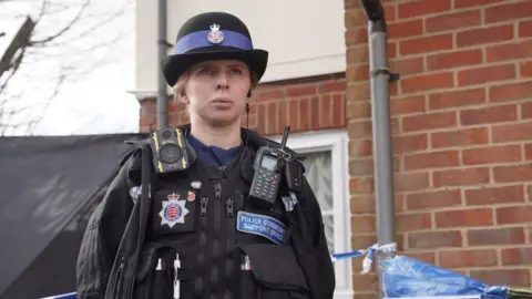 Essex Police A police community support officer stands in front of a cordoned-off property