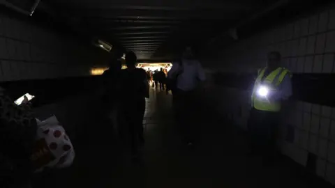 PA Media People walking in complete darkness at Clapham Junction station in London during a power cut,