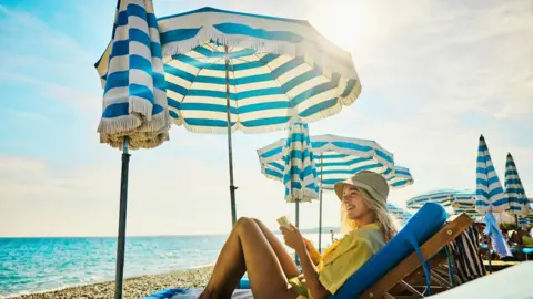 Getty Images A woman sits on a sun lounger under a sun umbrella