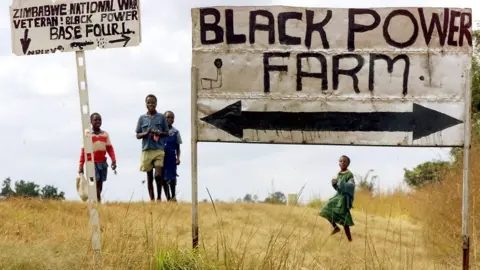 AFP Schoolchildren pass the entrance to an occupied farm outside Harare, Zimbabwe - 2000