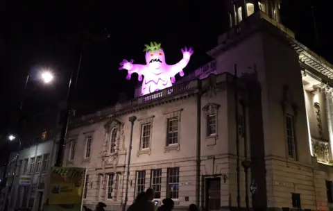 BBC A purple monster at the top of a building