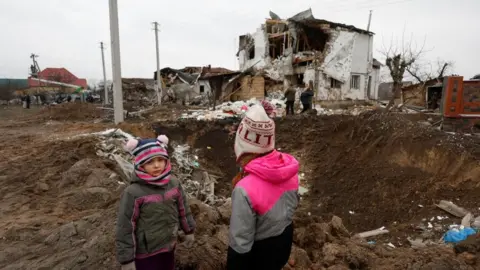 Reuters Kids stand next to a crater left by a Russian military strike in the town of Hlevakha, outside Kyiv