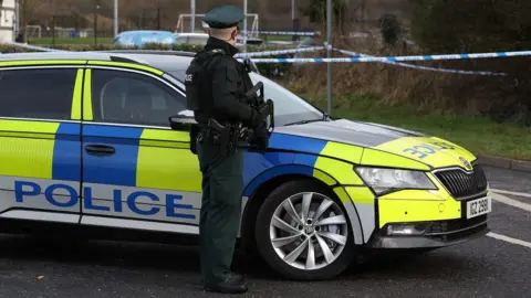 PA Media PSNI officer standing in front of a car holding a gun