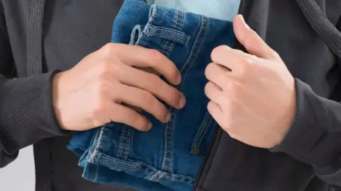 Getty Images Person shoplifting a pair of jeans