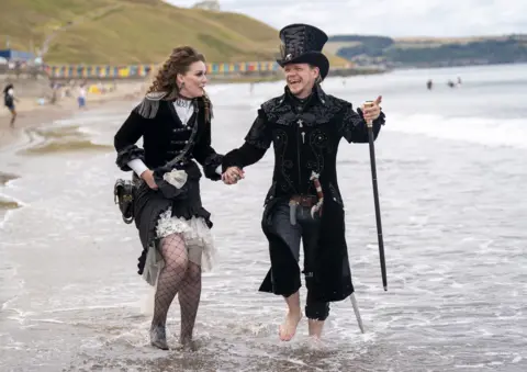 PA Media Emma Parfett and Shaun Smith paddle in the sea during the Whitby Steampunk Weekend