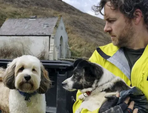 RNLI/Jordan Summersgill Ed Thomas holding the Jack Russell next to his dog Olly