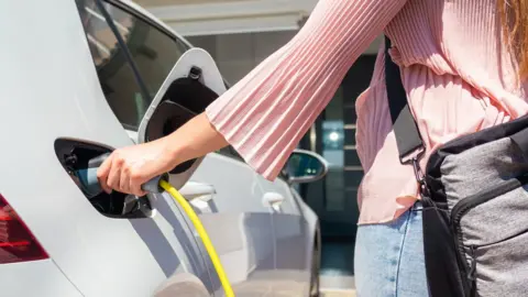 Getty Images Woman charging an electric car