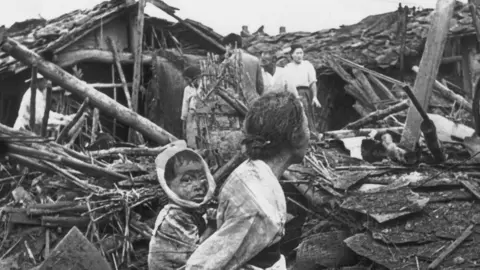 Getty Images An elderly woman and her grandchild wander at their wrecked home in the aftermath of an air raid over Pyongyang, circa 1950