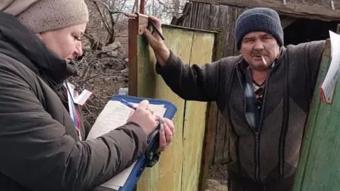 Russian-controlled Donetsk election commission A woman with a clipboard gives a man in occupied Ukraine voting papers