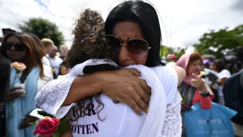 PA Media Two women hug as they attend the vigil in Ilford