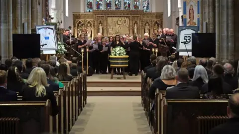 PA Media A choir singing around Barnaby's coffin