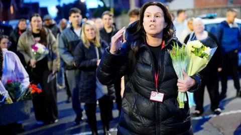 PA Media Leanne Reynolds holding flowers talking in a dark puffer jacket