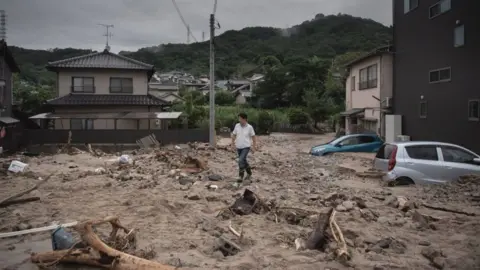 Getty Images Man walks past a devastated street during floods in Saka