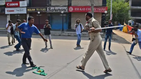 Getty Images A police officer tries striking a Kashmir Shiite mourner during the procession. Authorities in parts of Srinagar imposed strict restrictions to prevent Shiite Muslims from taking part in Muharram procession.