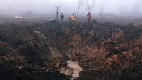 EPA Locals gather around a shelling crater after a rocket hit the Pisochyn neighborhood outside Kharkiv