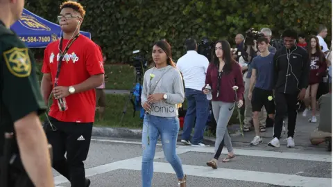 Getty Images Students walk across a road holding flowers as they arrive at Marjory Stoneman Douglas high school