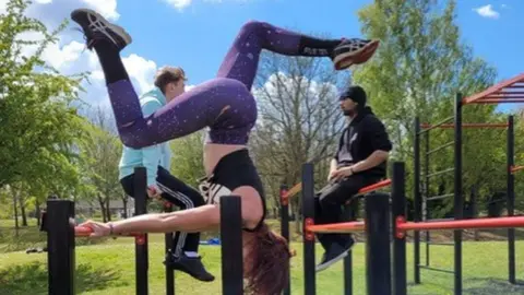 Nadia Gyane/BBC Woman using calisthenics on play equipment in a park in Wellingborough