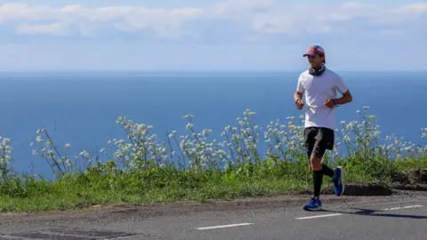 Nick Butter running on a road with the sea in the background