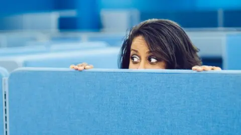 Getty Images Woman peeping over office divider