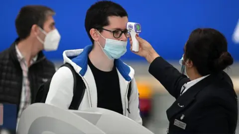 AFP Passengers have their temperature checked when checking in for flights at Heathrow Airport