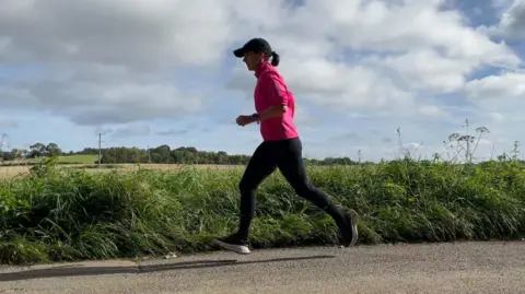 Woman in cap and pink top runs past field