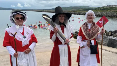 Women in traditional Welsh dress hold the Commonwealth Games baton