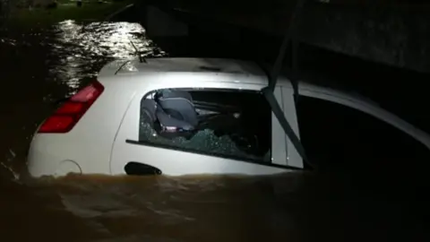 A white car with the window smashed and a child's car seat in the back