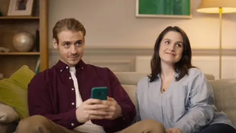 Flutter/ Paddy Power Still from Paddy Power ad showing a man sat next to his girlfriend whilst holding his phone in both hands