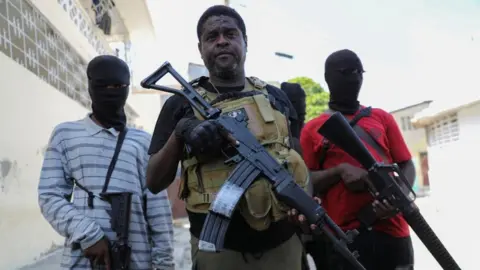 Reuters Former police officer Jimmy "Barbecue" Cherizier, leader of the 'G9' gang alliance, is flanked by gang members after a press conference in Delmas 6, Port-au-Prince, Haiti March 5, 2024.