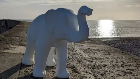 White unpainted elephant sculpture with the sea in the background