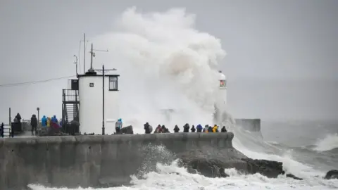 Ben Birchall/PA Wire People watch waves and rough seas pound against the harbour wall at Porthcawl