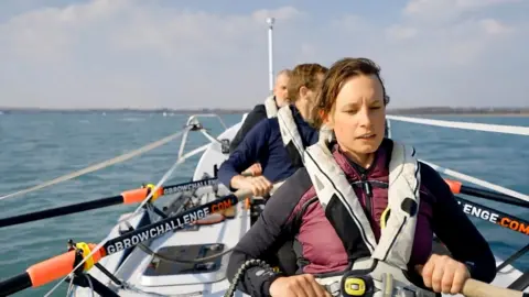 A woman and two men in an ocean rowing boat