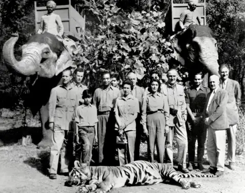 CENTRAL PRESS/AFP via Getty Images A black and white picture from 1961 shows the Queen, Prince Philip, the Maharaja and Maharani of Jaipur, India, and several others, standing in front of a tiger he had killed