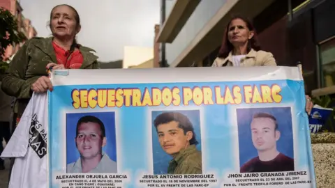 Getty Images Women hold a banner with the portraits of three men kidnapped by the FARC guerrilla, during a protest outside at the Special Jurisdiction for Peace (JEP) headquarters in Bogota on July 13, 2018.