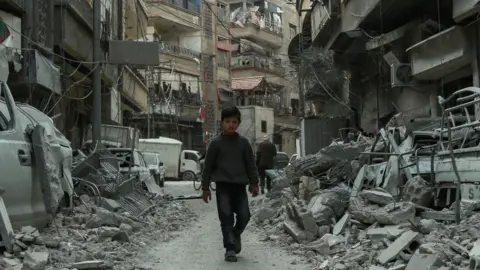 Syrian child walking down a street past rubble from destroyed buildings, in the rebel-held town of Douma in the Eastern Ghouta