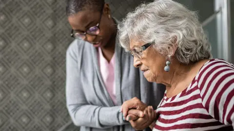 Getty Images A stock image of an elderly woman being supported by a carer as she walks