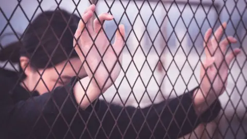 Getty Images Woman placing hands on wire fence (stock image)