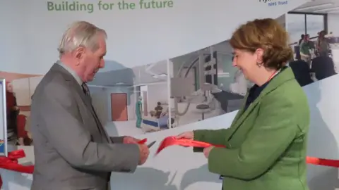 University Hospitals Plymouth NHS Trust Robert Jones, 96, cutting a red ribbon with trust chief executive Ann James