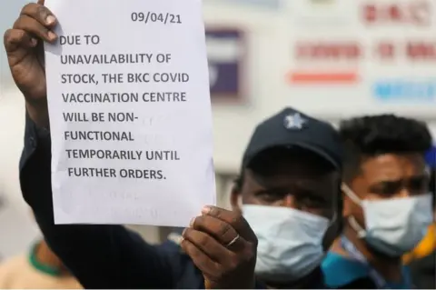 Reuters A guard holds up a notice to inform people about the shortage of coronavirus disease (COVID-19) vaccine supplies at a vaccination centre, in Mumbai, India, April 9, 2021.