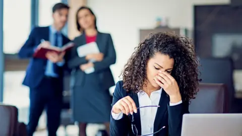 Getty Images A woman in the workplace under pressure, as two colleagues talk behind her back