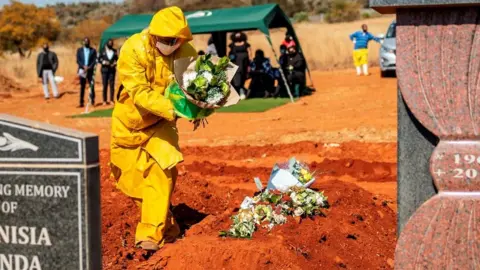 Getty Images An undertaker wearing personal protective equipment (PPE) lays flowers on the grave containing the remains of Modise Motlhabane, who died of COVID-19 coronavirus, during the funeral at the Westpark cemetery in Johannesburg, on July 22, 2020.