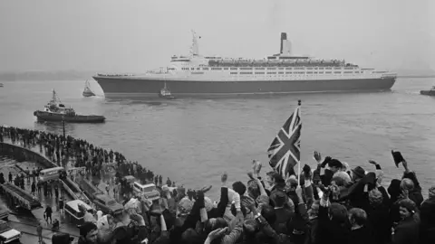 Potter Crowds wave from the quayside as the QE2 sets out on its maiden voyage from Southampton to New York