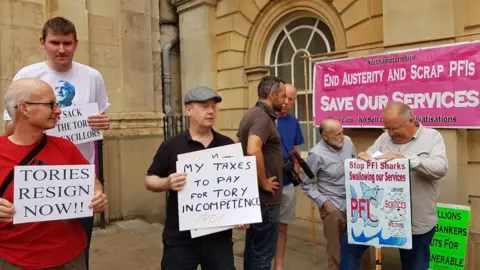 BBC About 20 people gathered outside County Hall to protest against cuts.